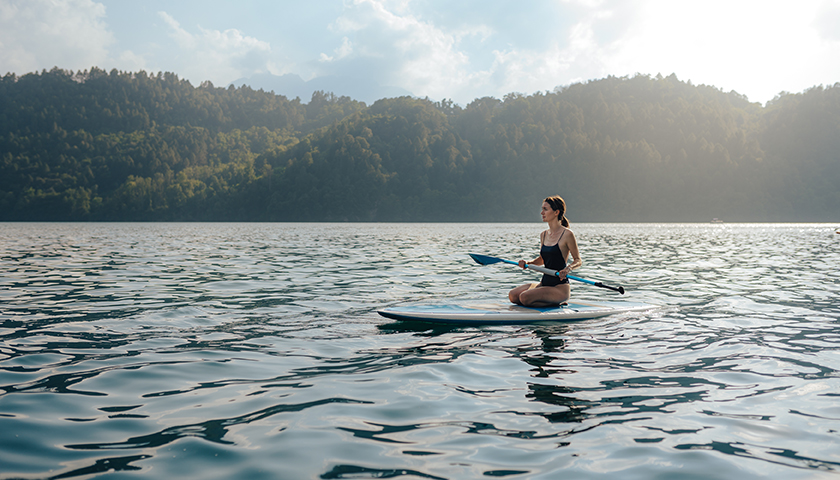 Ragazza in ginocchio su tavola SUP che osserva il lago